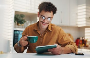 Home, coffee and man with tablet, smile and online reading with morning news, email and internet. Happy, tech and person in kitchen, connection and herbal tea with social media, digital app and latte